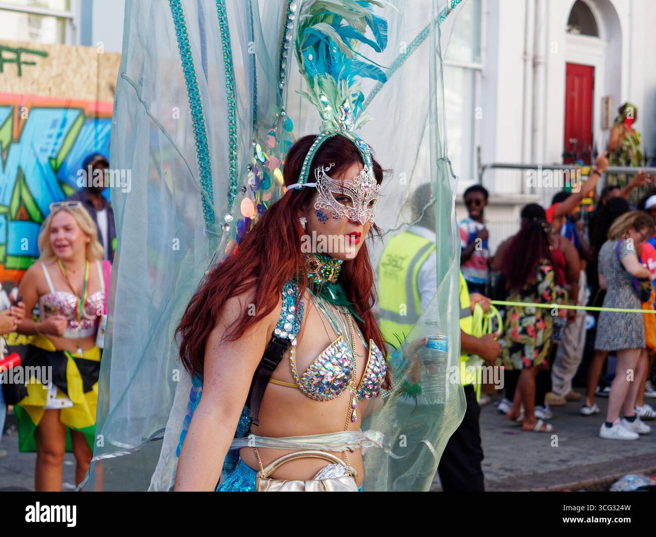 Femme sulfureuse avec coiffe/coiffe bleue et masque argenté et tenue de bikini pendant le Carnaval de Notting Hill, Londres. Angleterre 25 août 2025 Banque D'Images