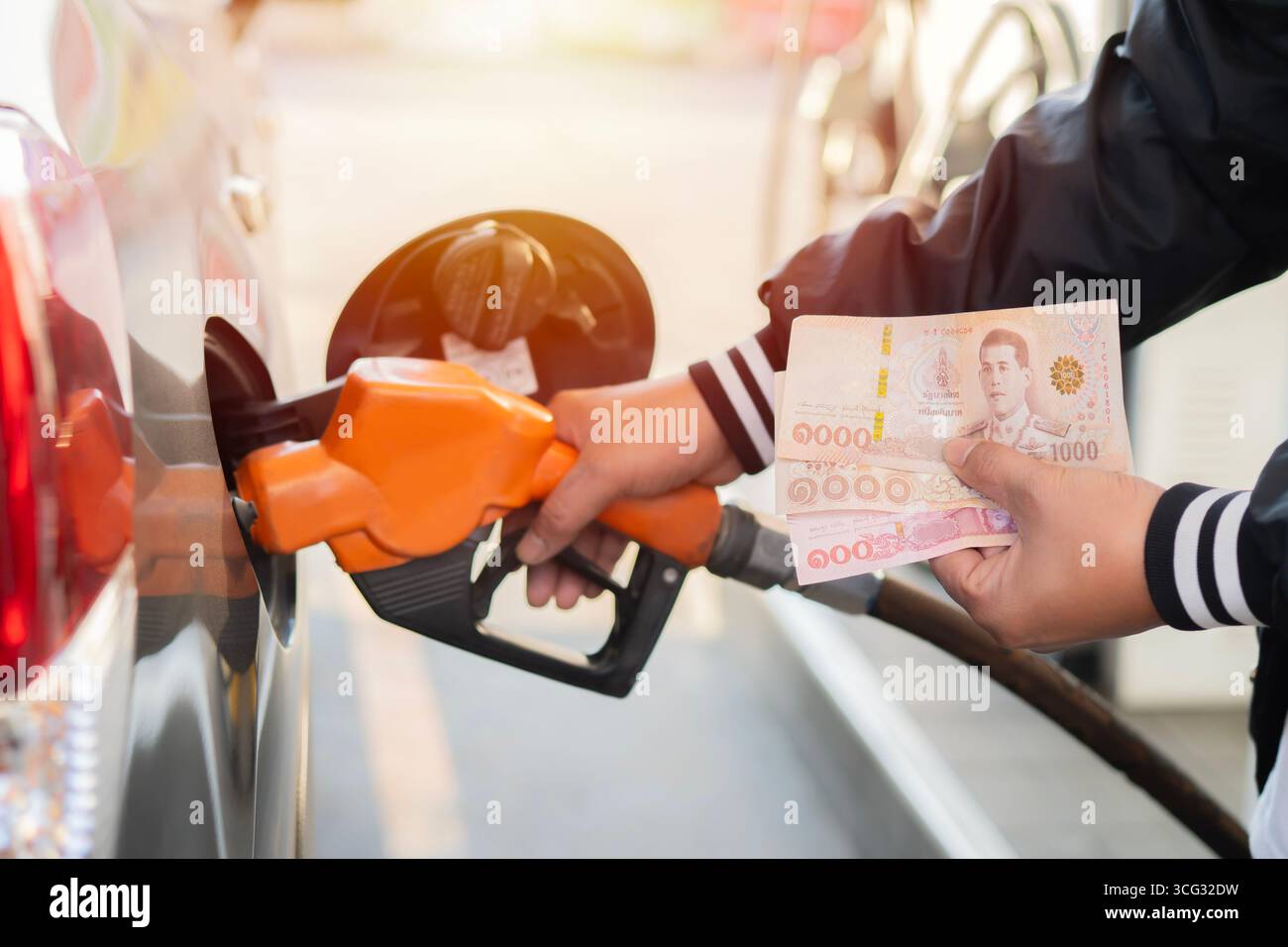 Main d'un homme ravitaillant la voiture et tenant deux mille billets de banque de cent baht, concept de hausse des prix du carburant. Banque D'Images
