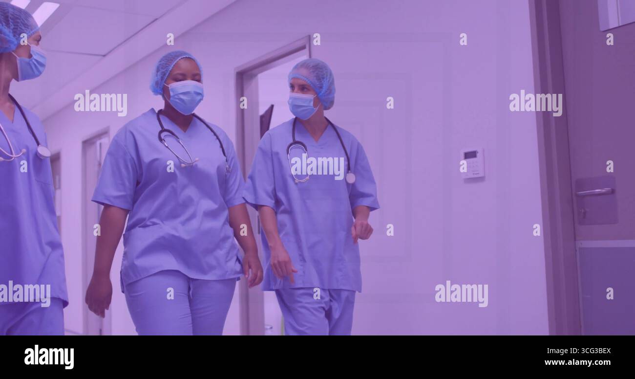 Marcher trois membres du personnel dans le couloir de l'hôpital portant des gommages bleus masques faciaux filets à cheveux avec stéthoscopes Banque D'Images