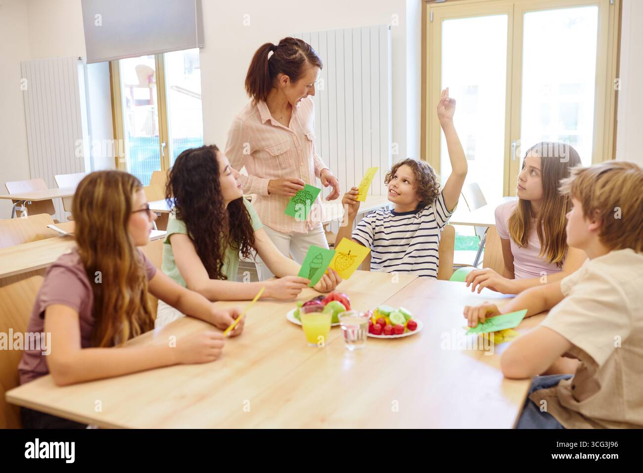 Un groupe diversifié d'élèves apprenant la nutrition avec leur professeur dans une cafétéria d'école lumineuse, présentant des produits frais et Interac éducatif Banque D'Images