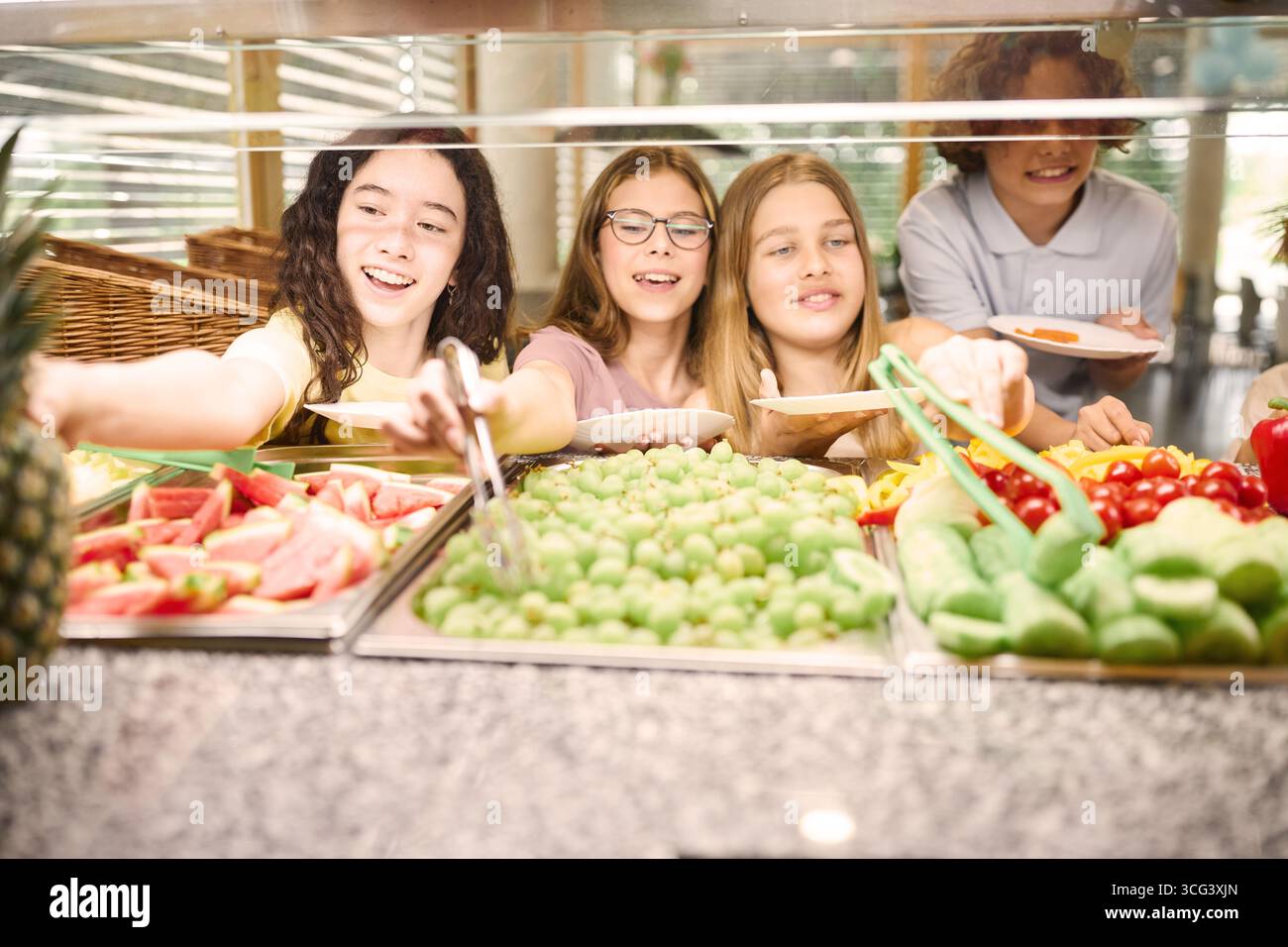 Groupe diversifié d'élèves sélectionnant des options d'aliments sains à partir d'une ligne de cafétéria d'école avec des légumes et des fruits frais. Scène vibrante et amicale emp Banque D'Images