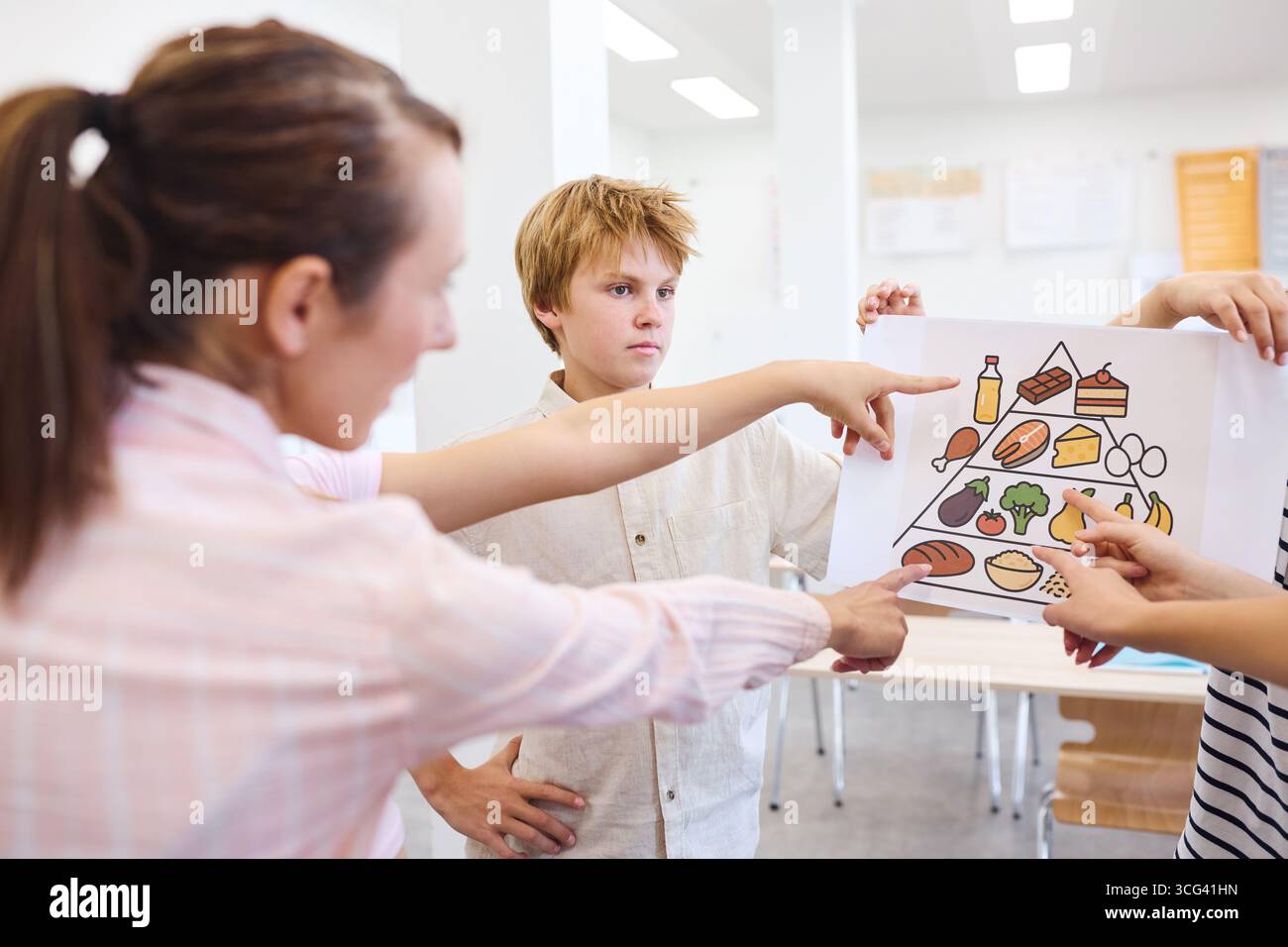 Un enseignant et des élèves discutent d'une alimentation saine à l'aide d'un diagramme pyramidal alimentaire. La leçon se déroule dans une salle de classe lumineuse, promouvant diverse et balan Banque D'Images