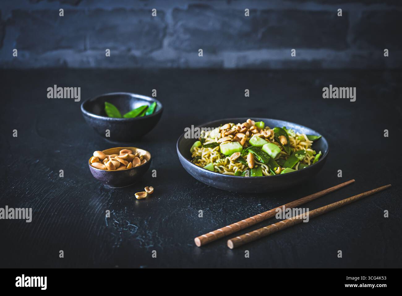 Nouilles asiatiques mie aux oignons de printemps et aux pois sucrés, garnies de concombre et de cacahuètes grillées sur fond noir Banque D'Images