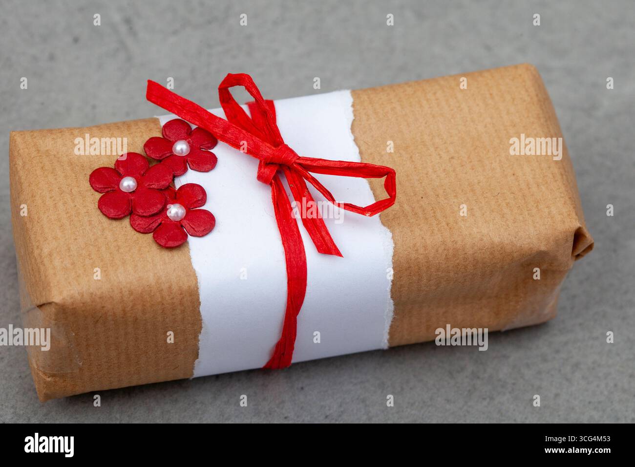 cadeau recouvert de papier brun et décoré de trois fleurs simples et d'un noeud rouge Banque D'Images