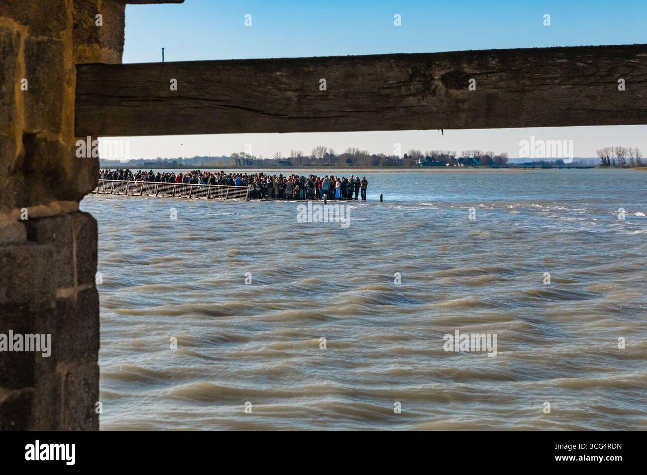 En regardant à travers la première porte d’entrée du Mont‑Saint‑Michel, la porte de l’avance, vers la baie inondée. Les visiteurs se rassemblent le long de la... Banque D'Images