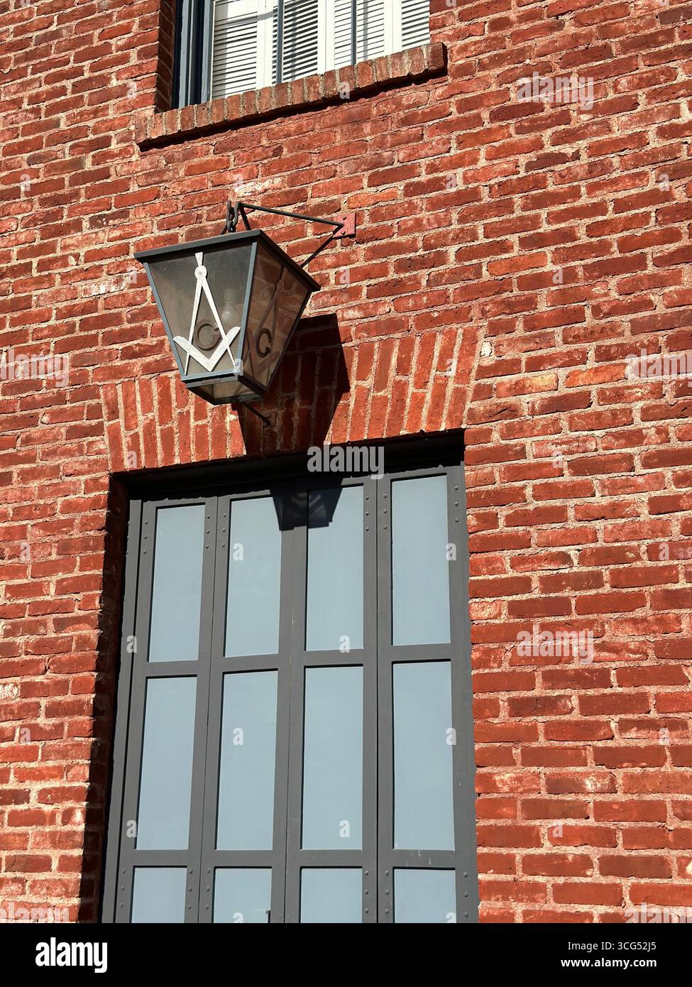 Une lanterne avec le symbole de la place franc-maçon et de la boussole est accrochée à l'extérieur d'un bâtiment historique en briques rouges. - Image de stock capturée avec un smartphone