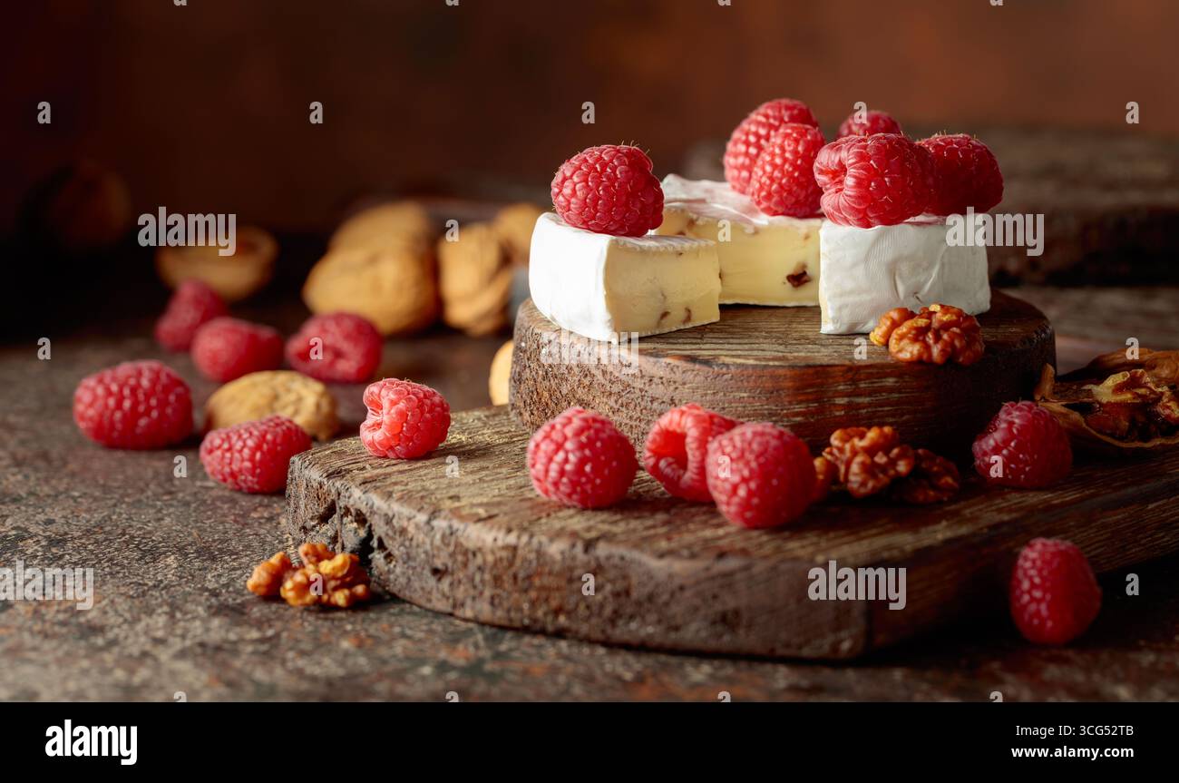 Camembert avec framboises fraîches et noix sur une table vintage brune. Banque D'Images