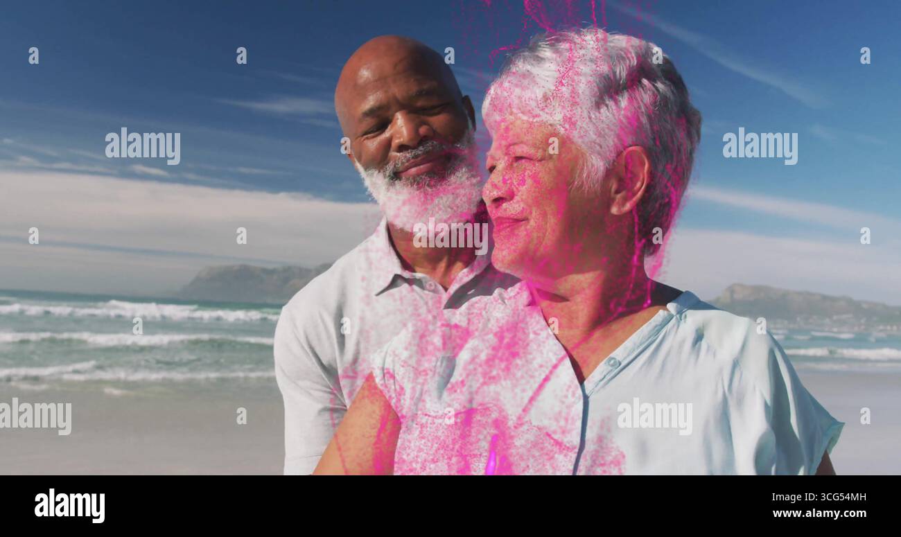 Enveloppant bras homme mature embrassant femme senior sur la plage de sable, avec des vagues de l'océan et des collines lointaines Banque D'Images