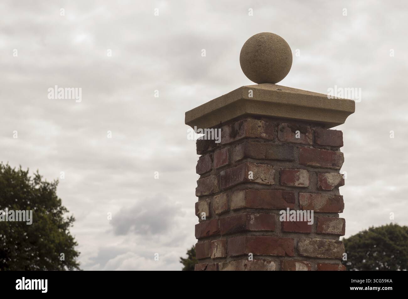 Pilier de brique supportant une sphère de pierre sous un ciel nuageux, suggérant un élément architectural classique Banque D'Images