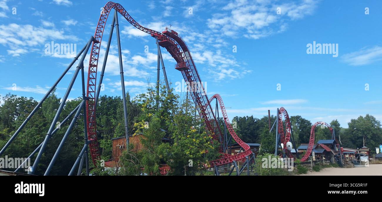 En milieu d'après-midi, les visiteurs profitent d'une balade palpitante sur une montagne russe torsadée entourée de verdure dans un parc d'attractions sous un ciel bleu vif Banque D'Images