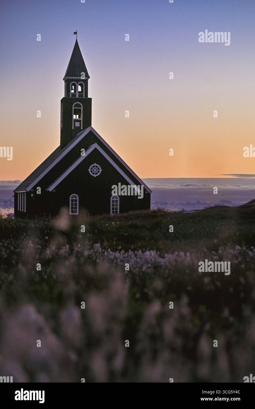 Église en bois au coucher du soleil entourée de fleurs arctiques à Ilulissat, Groenland Banque D'Images