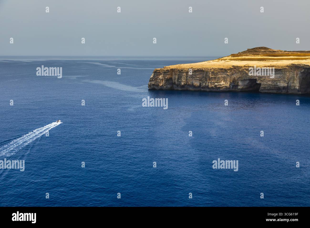 Un petit bateau laisse un sentier blanc sur la mer Méditerranée bleue près des falaises calcaires de Gozo Malta. Banque D'Images
