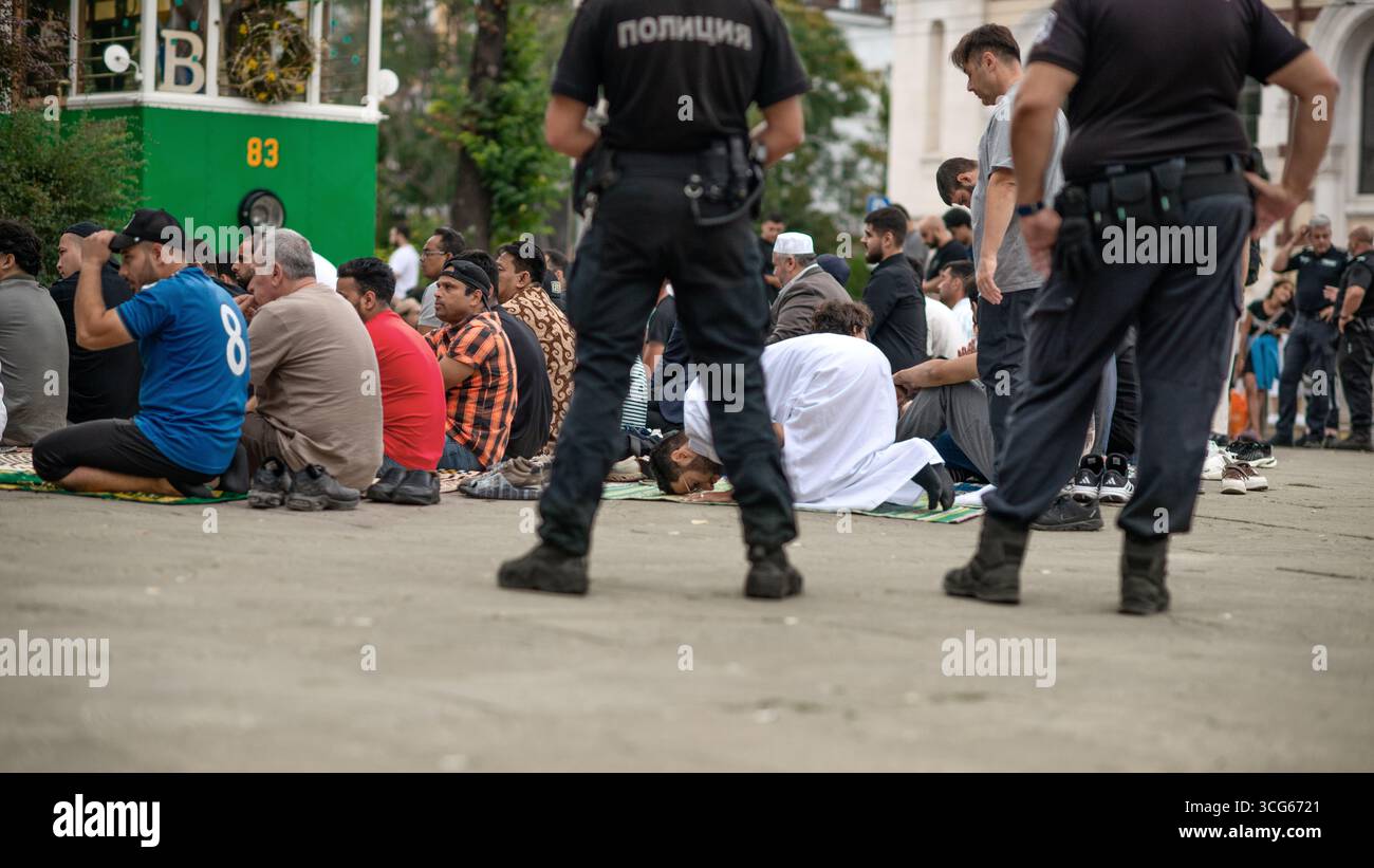 Prière du vendredi près de la mosquée Banya Bashi à Sofia, Bulgarie, avec des fidèles musulmans assis et prosternés sur des tapis sous la supervision de la police, réfléchissant Banque D'Images