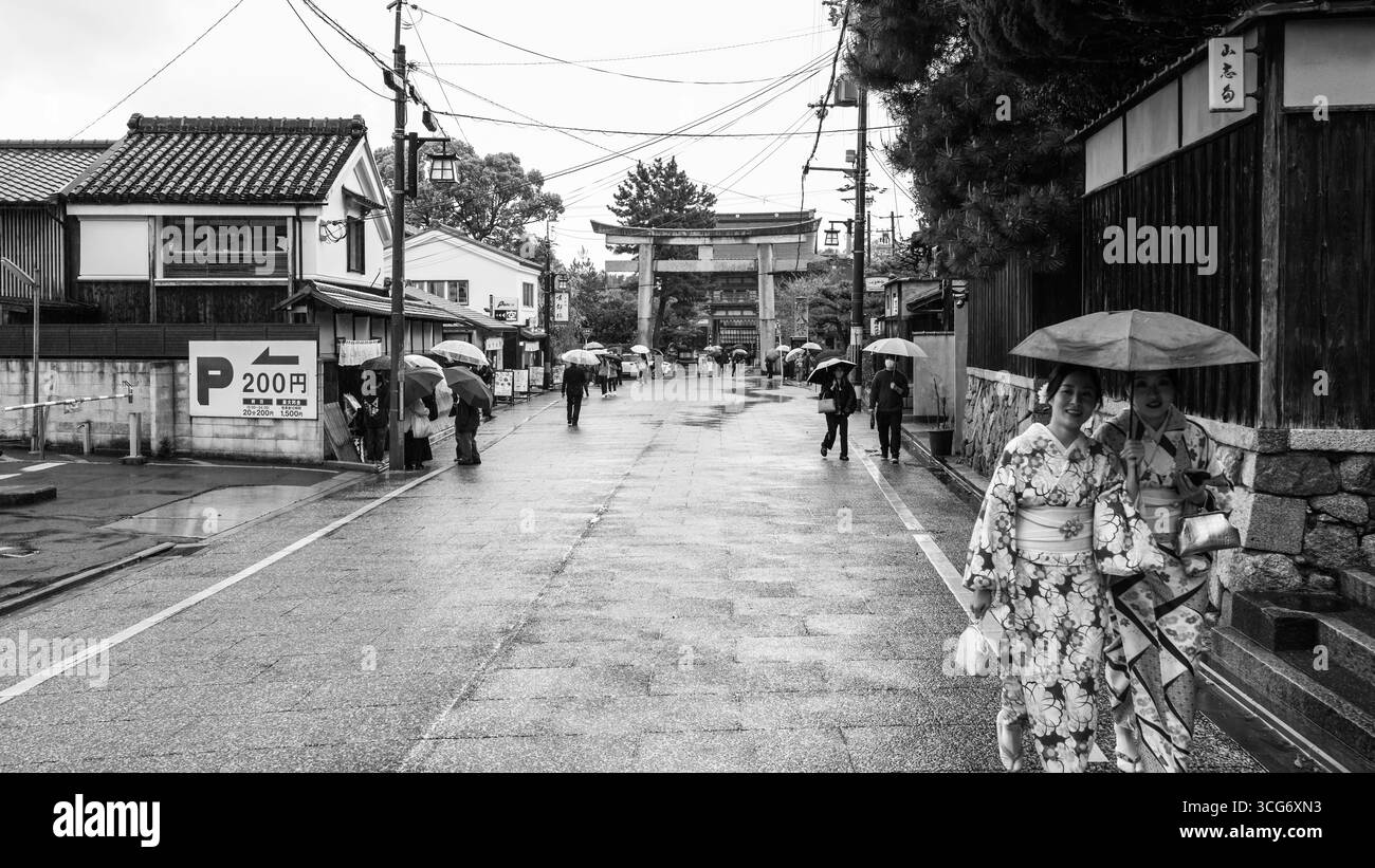 Scène de jour de pluie capturant des femmes dans une rue japonaise traditionnelle, portant des kimonos et tenant des parapluies, avec une porte Stone Torii en arrière-plan, sh Banque D'Images
