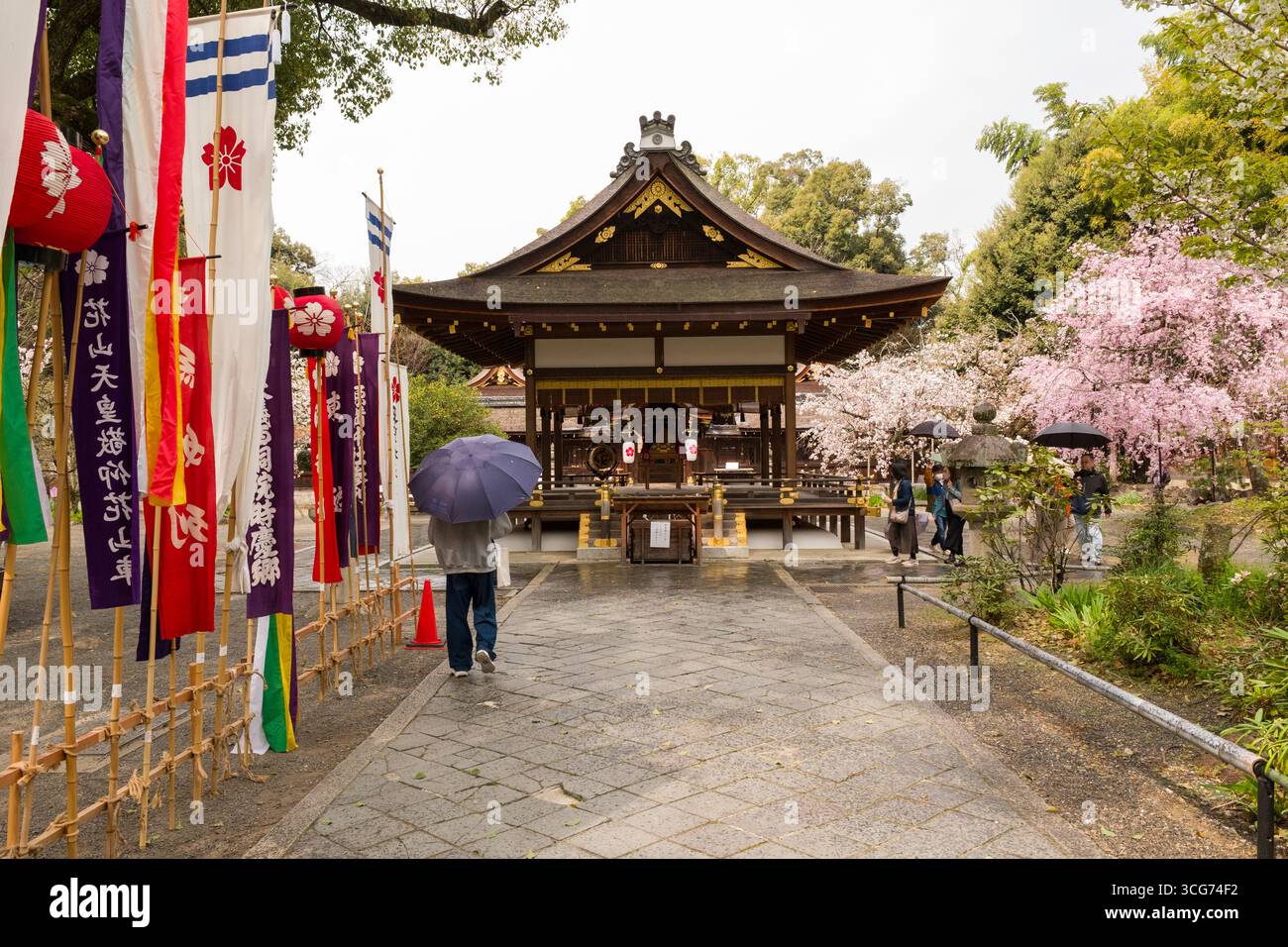 Un visiteur marche le long d'un sentier de pierre vers un Haiden traditionnel au sanctuaire Hirano, le sentier bordé de drapeaux et de bannières colorés, Kyoto, Japon Banque D'Images