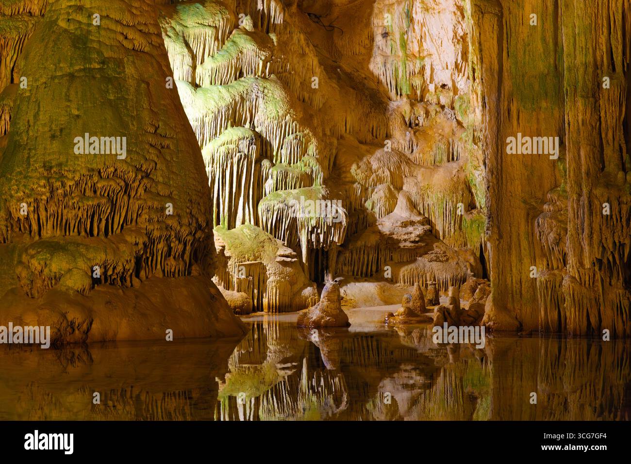 Spectaculaires formations de stalactites et de stalagmites dans la grotte de Neptune, en Sardaigne, se reflétant sur des eaux calmes aux teintes verdâtres et à l’éclairage doré. Banque D'Images