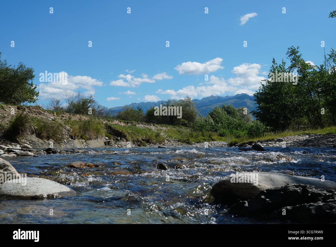 Rivière animée rapide avec de l'eau douce claire qui coule sur des pierres avec des arbres sur les rives et les montagnes et le ciel bleu dans la distance sur la journée ensoleillée d'été à TR Banque D'Images