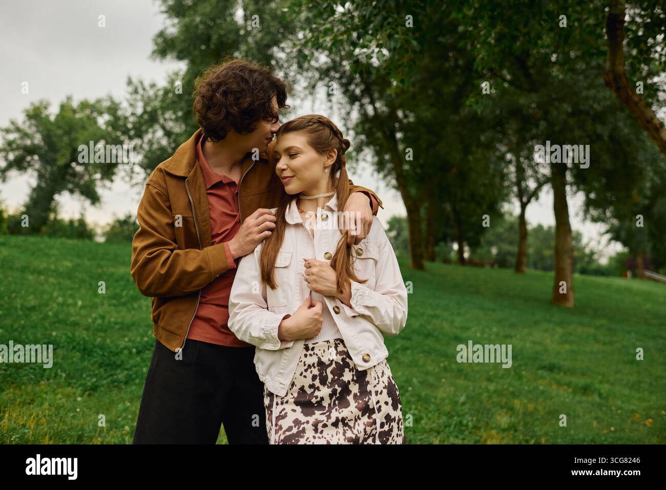 Un homme embrasse doucement un front de femme alors qu'ils se promènent dans un parc verdoyant luxuriant dans une harmonie heureuse. Banque D'Images