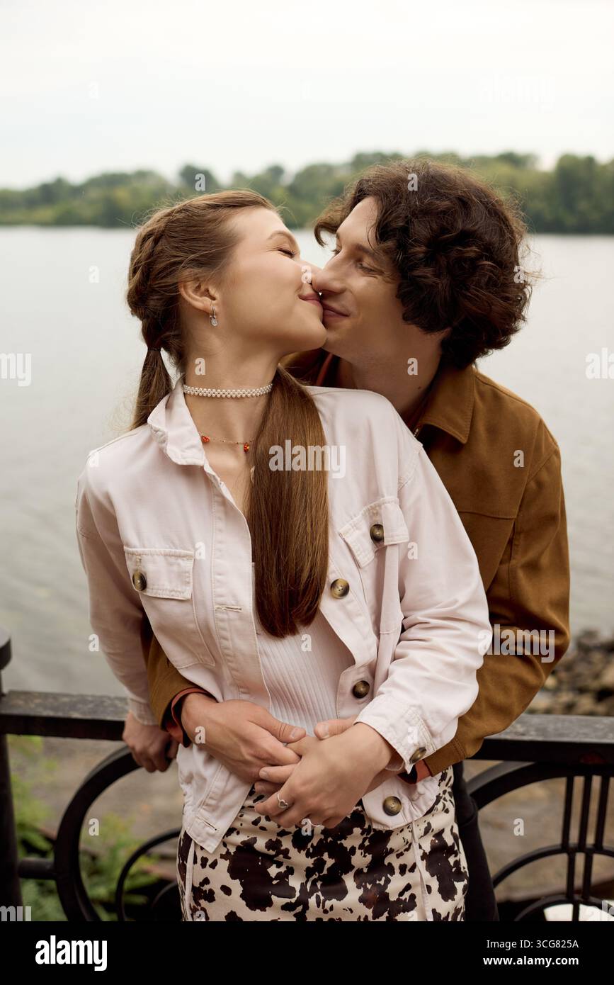 Un couple joyeux capte l'affection, profitant d'une promenade paisible près de l'eau dans un parc luxuriant. Banque D'Images