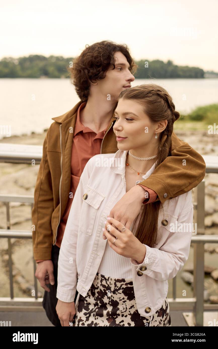 Un jeune couple partage un moment tendre en se promenant main dans la main au bord de l’eau, rayonnant de joie. Banque D'Images