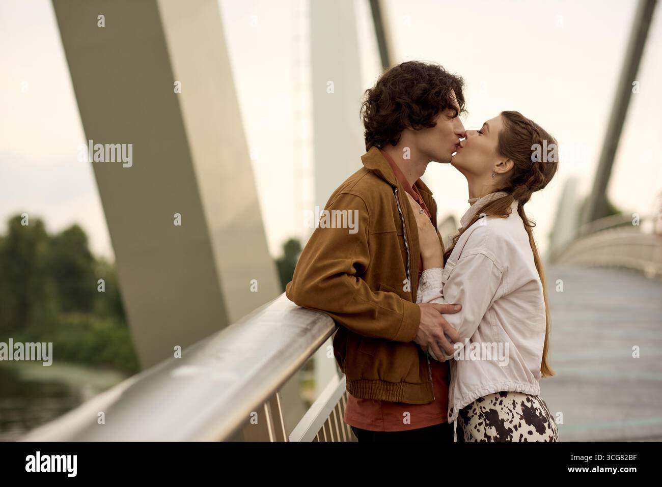 Jeune couple embrasse dans un moment d'amour tout en profitant d'une promenade sereine sur un pont. Banque D'Images