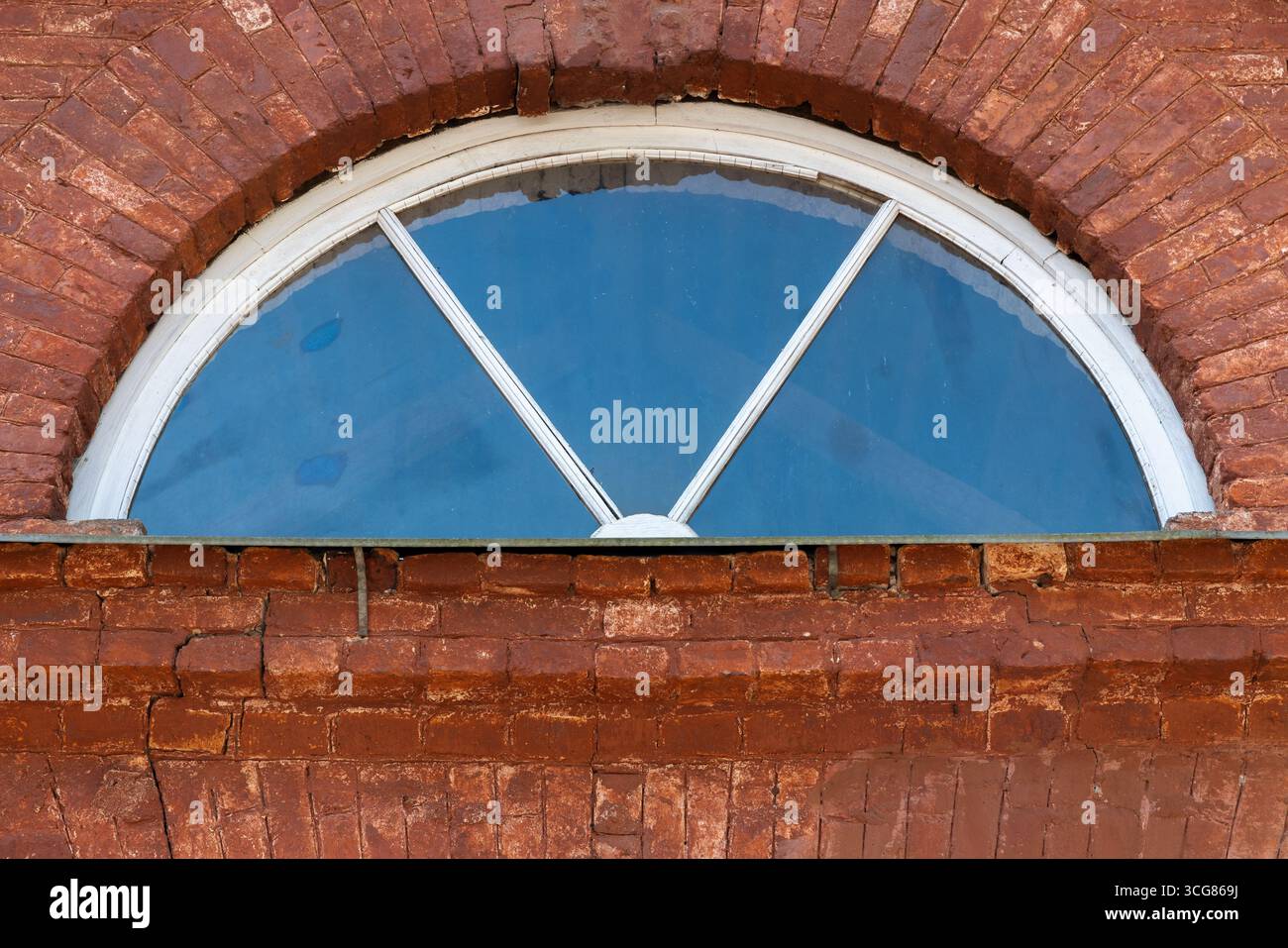 Design architectural rustique avec une fenêtre en forme de demi-cercle encastrée dans un mur de briques vintage, reflétant un ciel bleu qui ajoute charme et simplici Banque D'Images