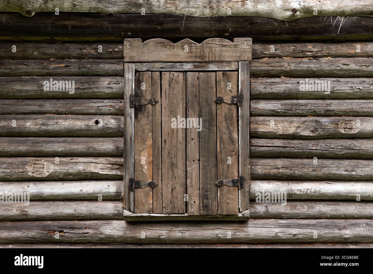 Une fenêtre en bois vintage avec volet fermé placé contre l'extérieur texturé d'une cabane en rondins rustique, représentant la simplicité et une ambiance rurale intemporelle Banque D'Images