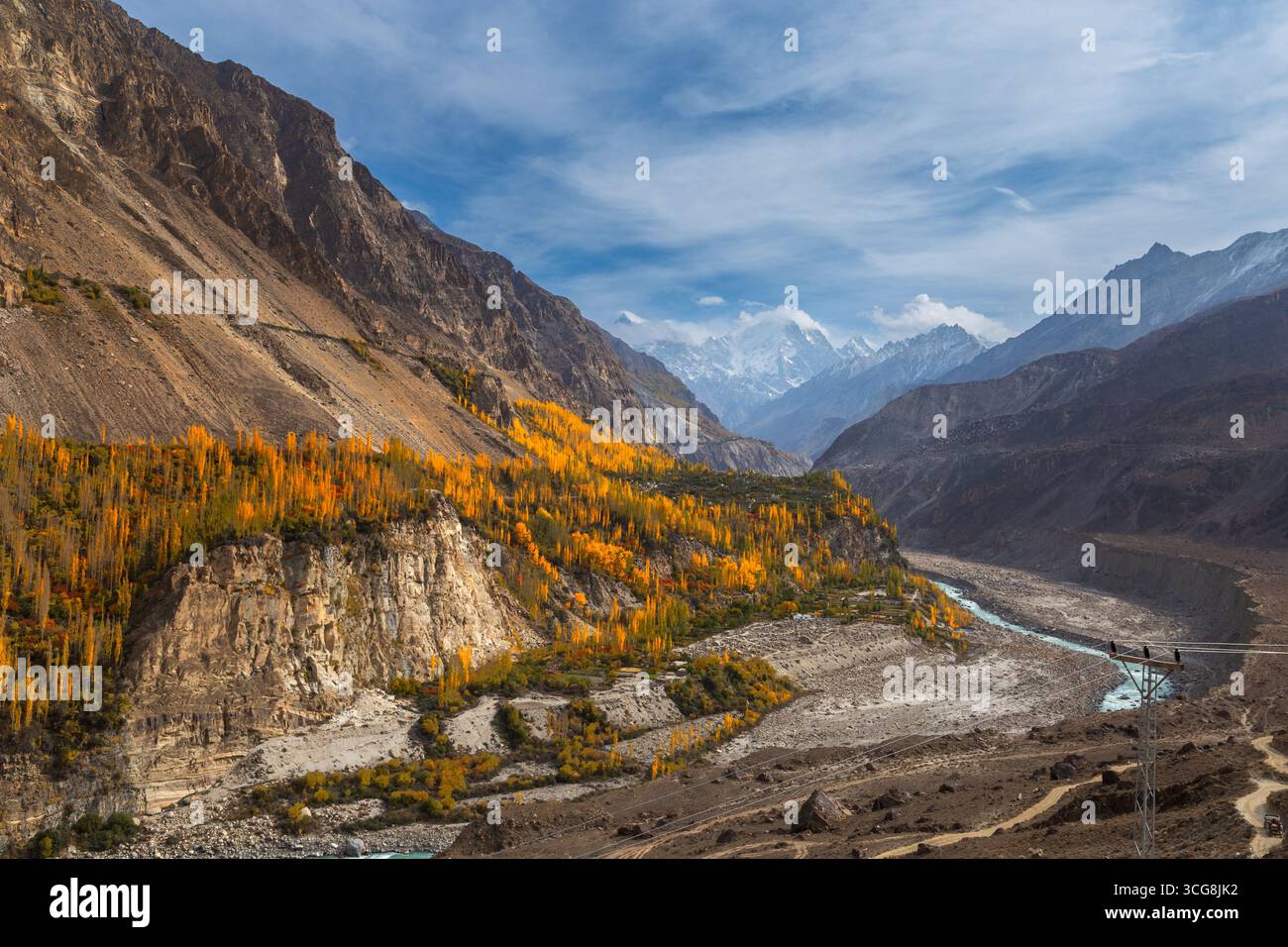 Vue d'arbres d'automne dorés accrochés à des falaises escarpées surplombant une rivière sinueuse sur fond de montagnes enneigées, Hunza Nagar, Gilgit Baltistan, Pakistan. Banque D'Images