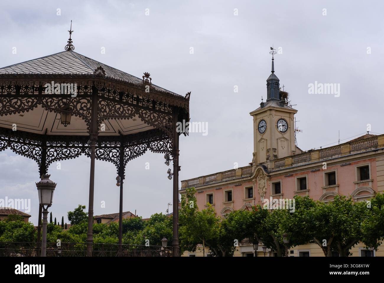 Vue d'un belvédère orné, un bâtiment avec une tour de l'horloge, et des arbres sous un ciel nuageux créent une scène urbaine sereine, Alcala de Henares, Communauté de Madrid, Espagne. Banque D'Images