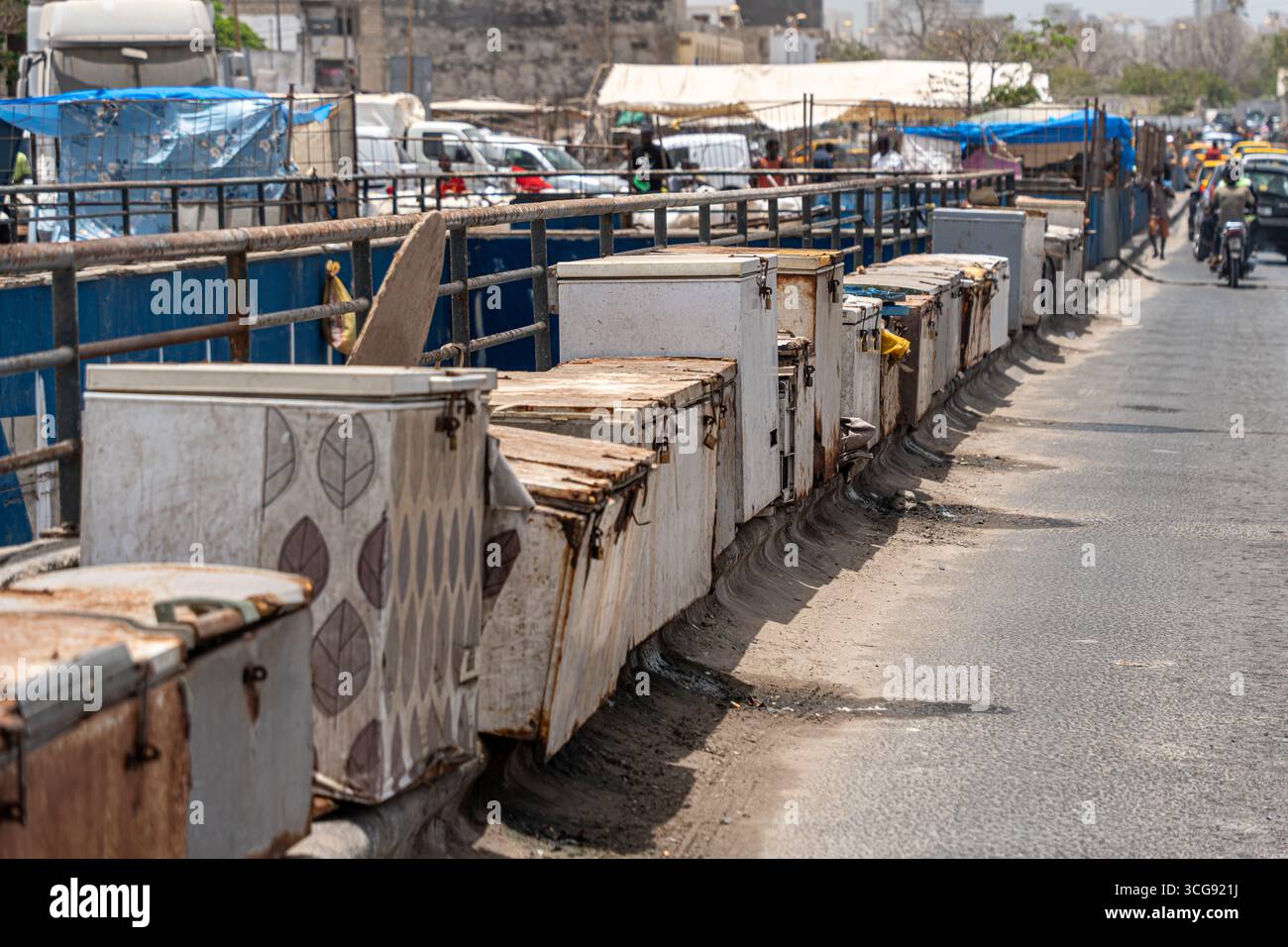 Dakar, Sénégal - 12 mai 2025 : vue de boîtes métalliques altérées bordant le pont de la plage de Soumbédioune, leurs motifs délavés contrastant avec l'animation de la ville en toile de fond. Banque D'Images