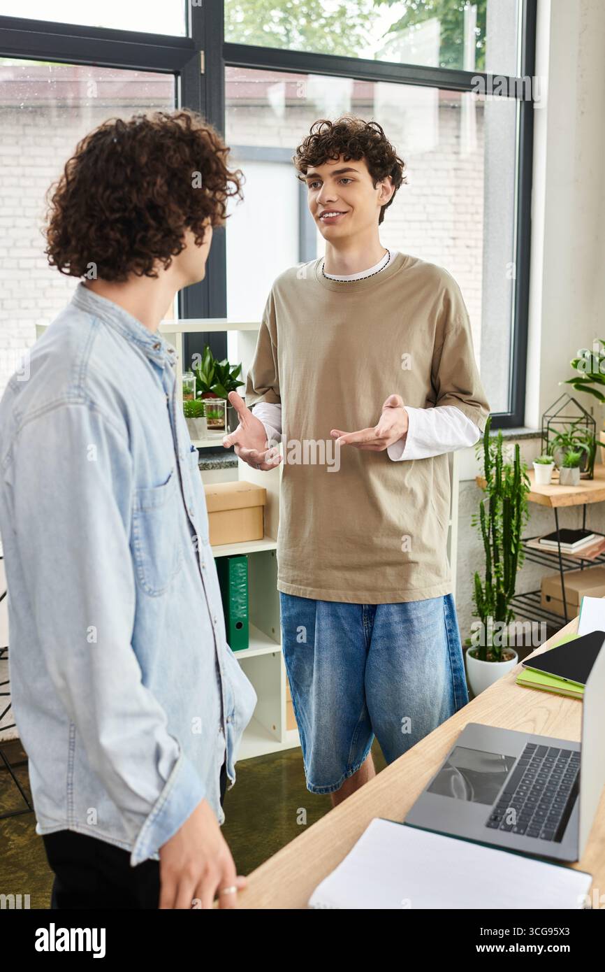 Deux jeunes personnes s’engagent dans une discussion collaborative tout en travaillant dans un bureau lumineux. Banque D'Images