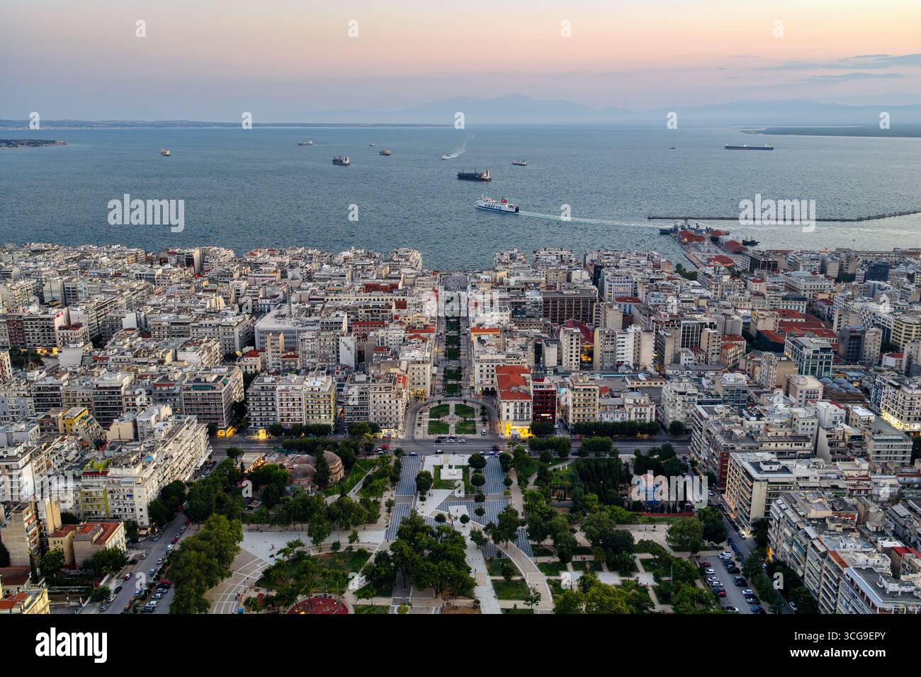 Thessalonique, Grèce 3 août 2025. Vue aérienne drone du centre-ville au coucher du soleil avec ciel rose, architecture urbaine, navires dans le golfe Thermaic et par vert Banque D'Images