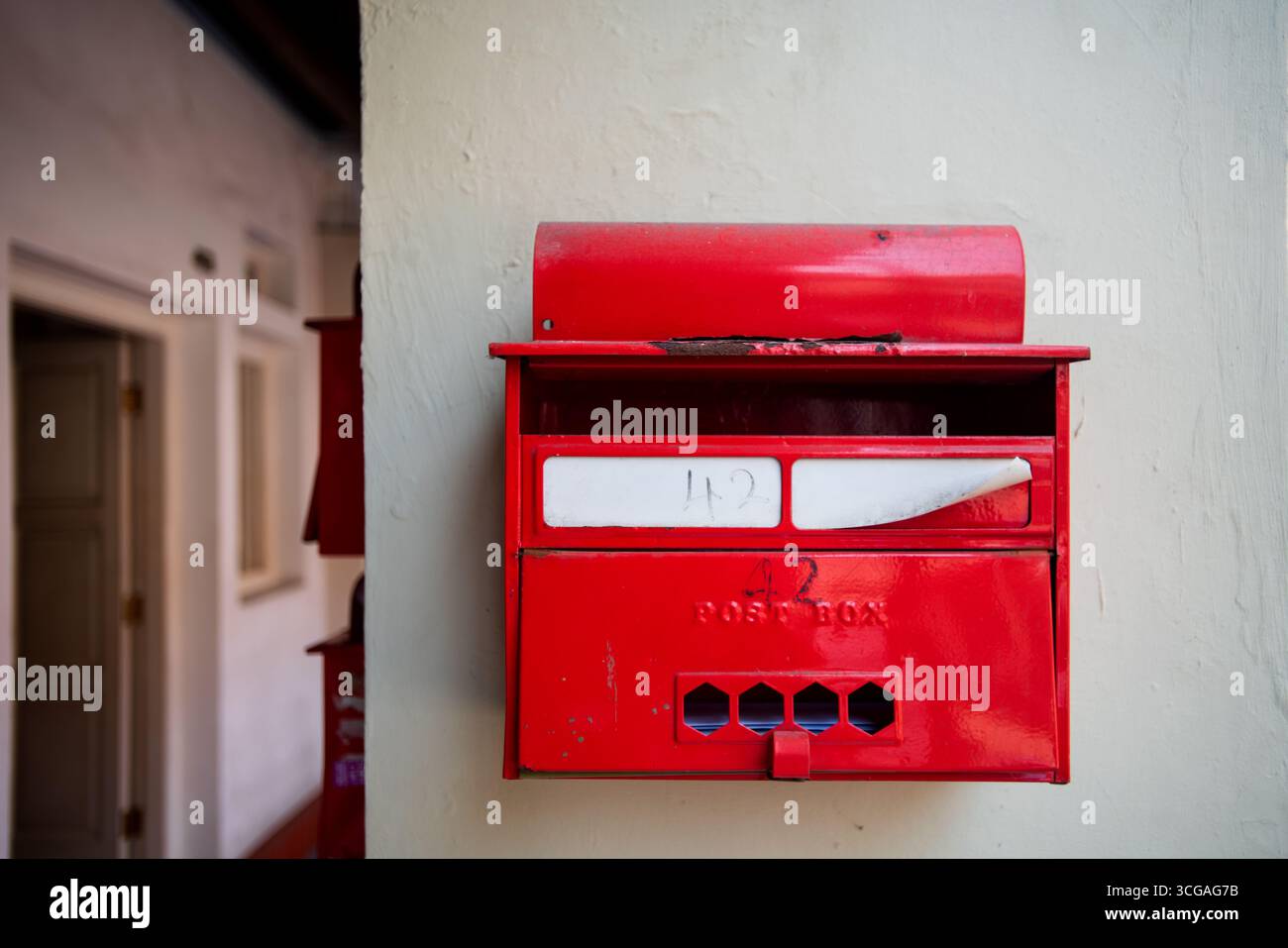 Une boîte aux lettres rouge est montée sur un mur, avec du courrier visible à l'intérieur et de la peinture légèrement usée sur le couvercle supérieur. Banque D'Images