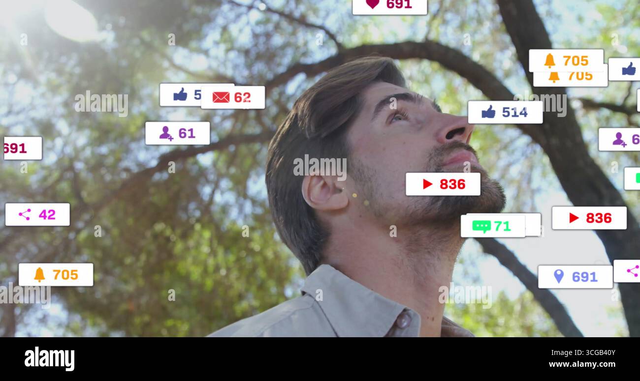 Homme adulte debout portant une chemise boutonnée dans le parc sous les arbres, avec des icônes de notification flottantes Banque D'Images