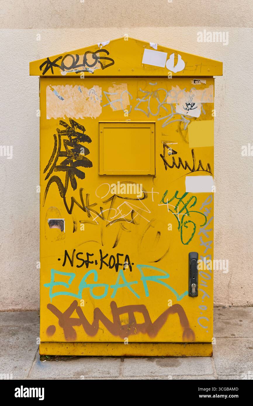 Gros plan urbain d'un boîtier électrique de rue jaune vif entièrement recouvert de graffiti noir, bleu et brun, monté sur un mur lumineux avec un petit verrou Banque D'Images