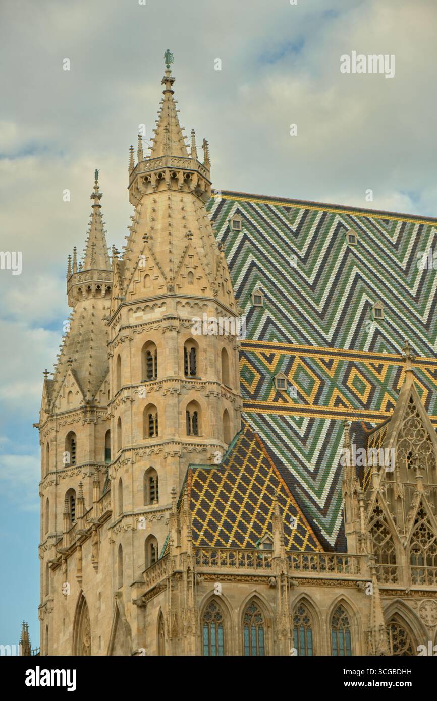Vue de : Cathédrale d'Étienne à Vienne avec son toit en mosaïque colorée et ses flèches avant contre un ciel partiellement nuageux, mettant en évidence l'archite gothique Banque D'Images