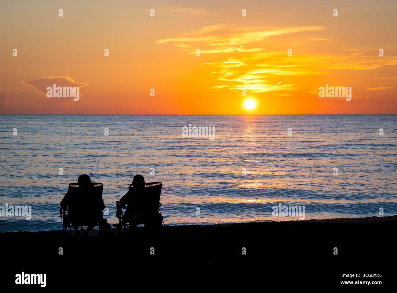 Couple assis sur la plage regardant le coucher du soleil sur le golfe d'Amérique, anciennement le golfe du Mexique, de Vencie Beach à Vencie Florida USA Banque D'Images