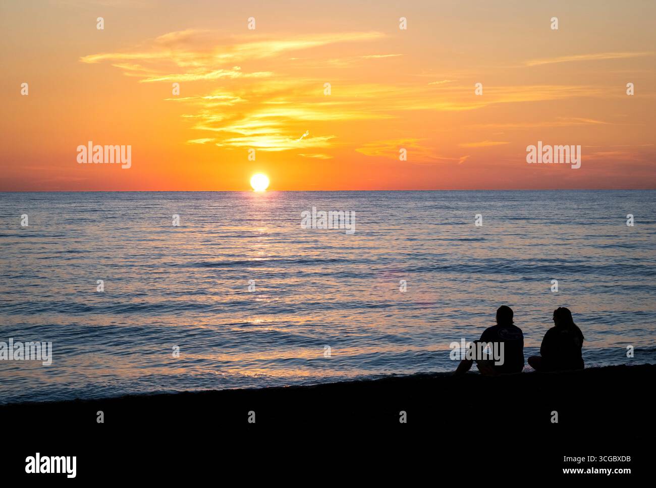 Couple assis sur la plage regardant le coucher du soleil sur le golfe d'Amérique, anciennement le golfe du Mexique, de Vencie Beach à Vencie Florida USA Banque D'Images