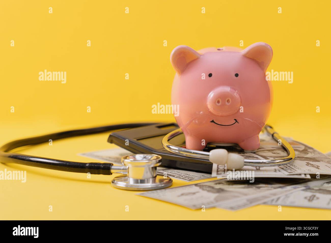 Tirelire rose sur la calculatrice avec des billets de dollar dispersés et stéthoscope sur fond jaune. Banque D'Images