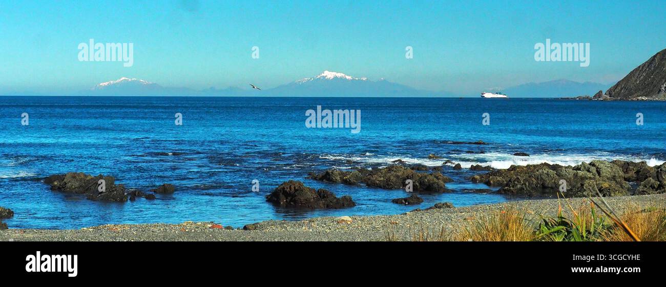 De la baie d'Owhiro dans l'île du Nord, en regardant à travers le détroit de Cook jusqu'à la chaîne enneigée de Kaikoura avec un ferry Interislander au loin. Banque D'Images