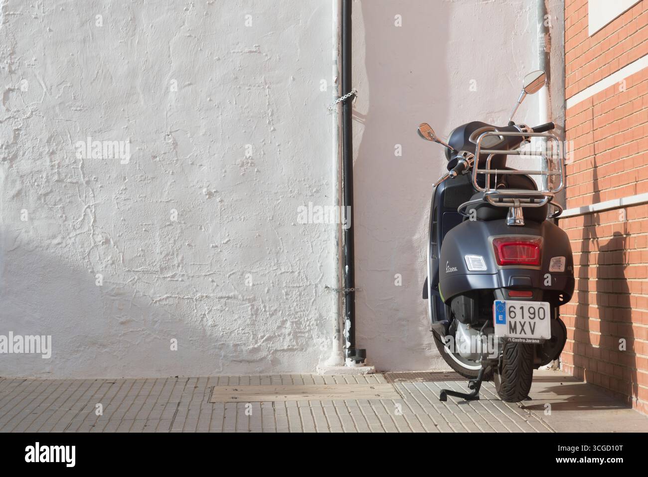 Moto Vespa bleu métallisé garée sur le trottoir devant un mur blanc Banque D'Images