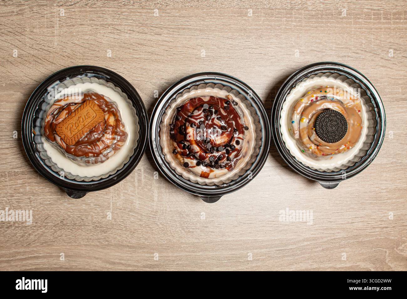 Une vue de haut en bas d'un assortiment de trois petits pains gourmands à la cannelle dans une rangée avec différentes garnitures sur un fond en bois clair parfait pour les menus ou DEL Banque D'Images