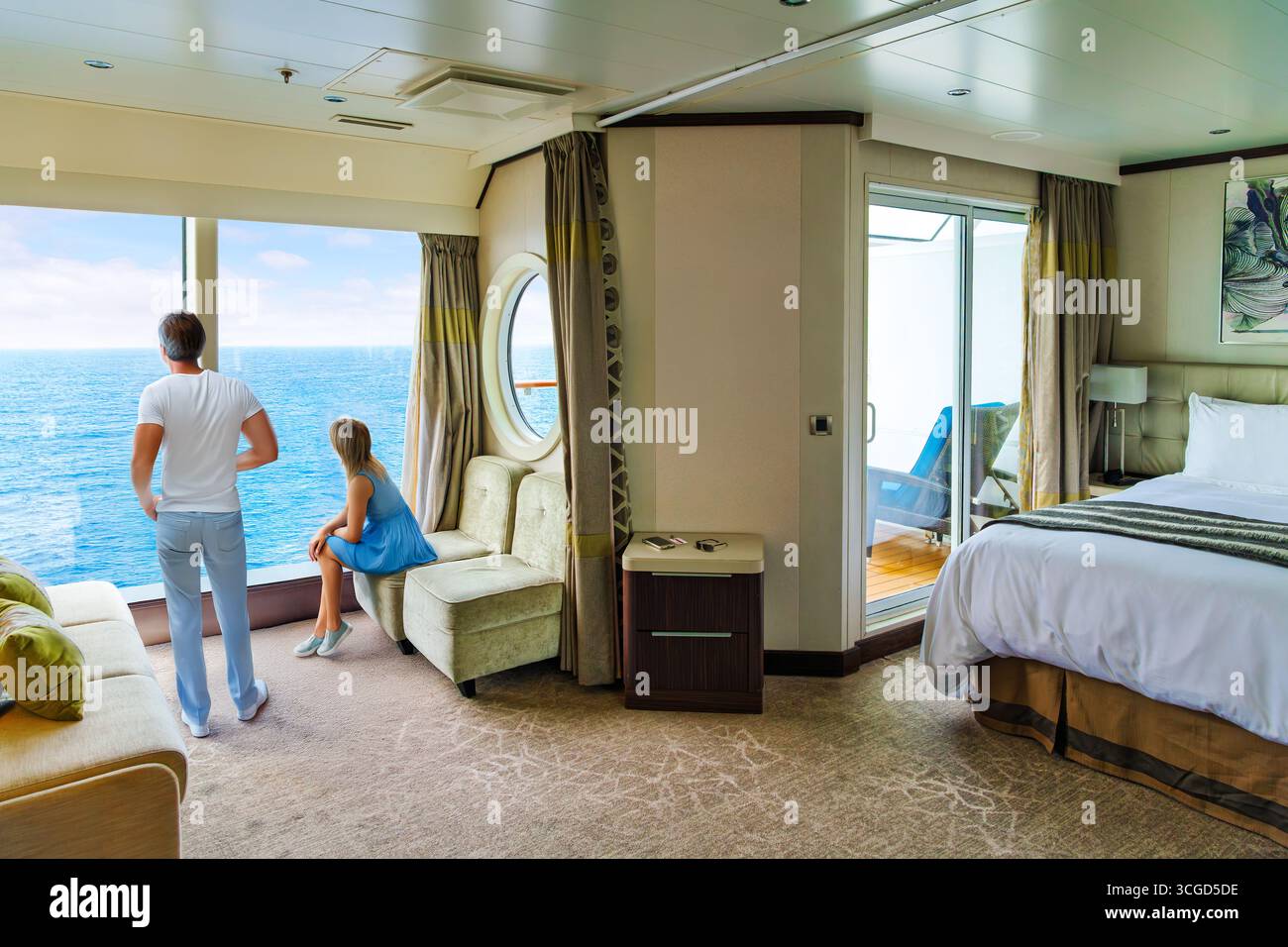 Un couple profite de la vue sur la mer depuis une baie vitrée dans leur luxueuse suite avec balcon sur un bateau de croisière en mer. Banque D'Images