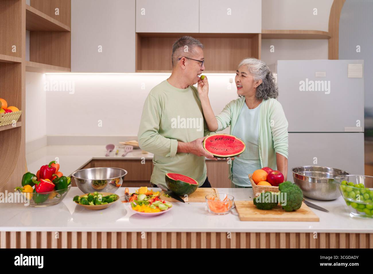 Joyeux couple asiatique senior partage un moment heureux en préparant des fruits et légumes frais vibrants dans un concept de repas sain de cuisine maison moderne et lumineux Banque D'Images