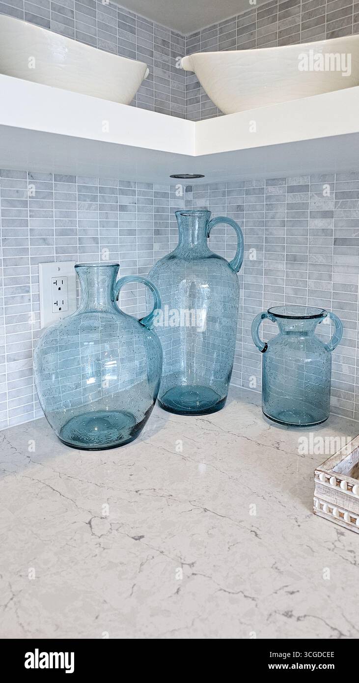 Trois vases en verre bleu de différentes tailles sont disposés sur un comptoir en marbre, ajoutant une touche d'élégance à la décoration contemporaine de la cuisine Banque D'Images