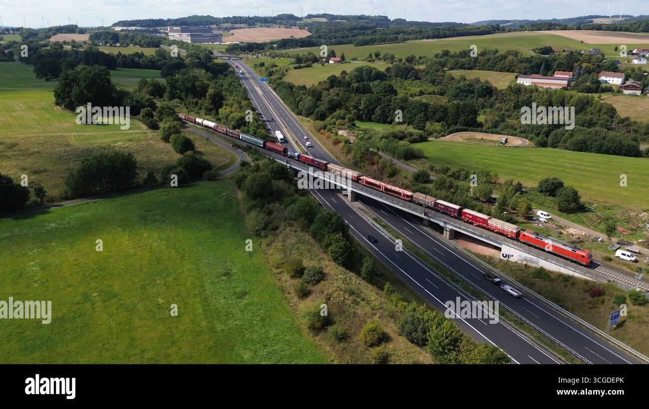 Drone vue du pont traversant le train de marchandises sur l'autoroute très fréquentée dans la campagne rurale avec des champs et des collines Banque D'Images