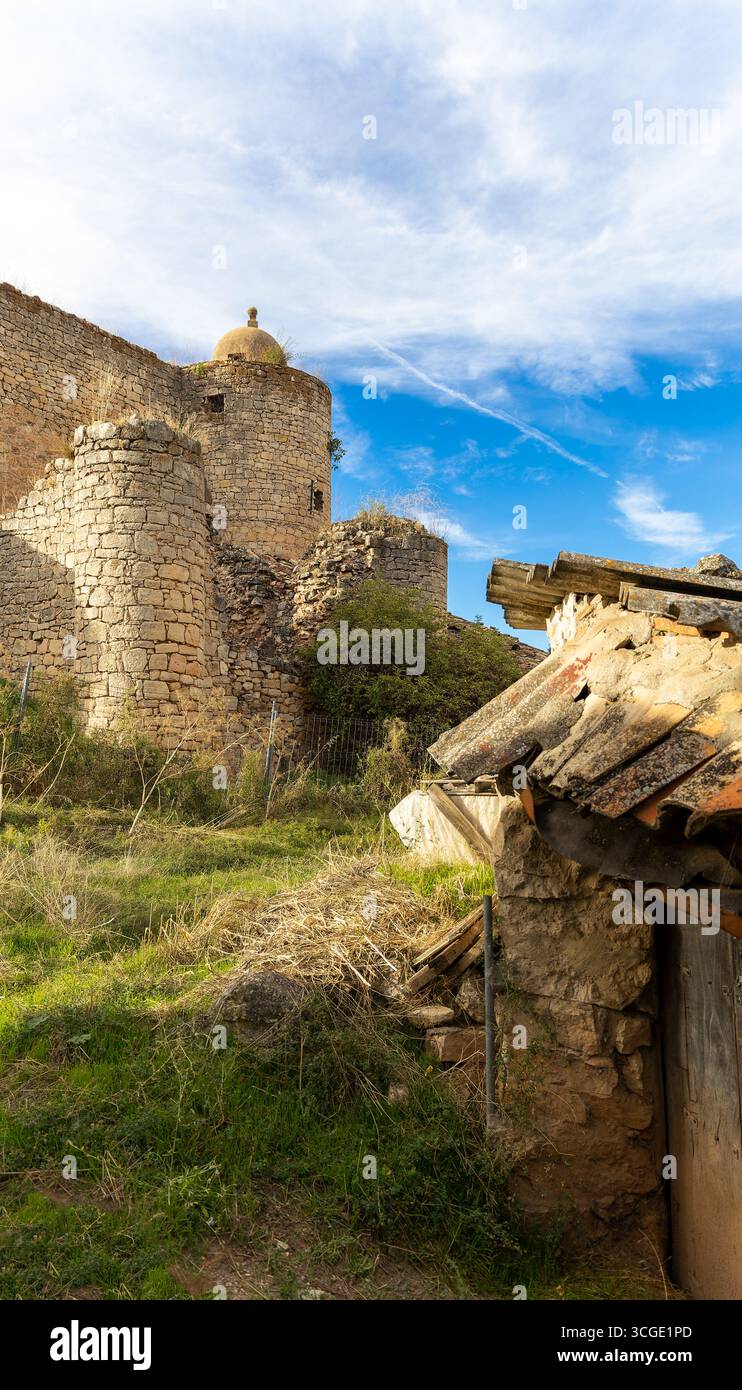 Ruines d'un bâtiment médiéval en pierre avec un toit et une petite maison. Le ciel est bleu et l'herbe est verte Banque D'Images