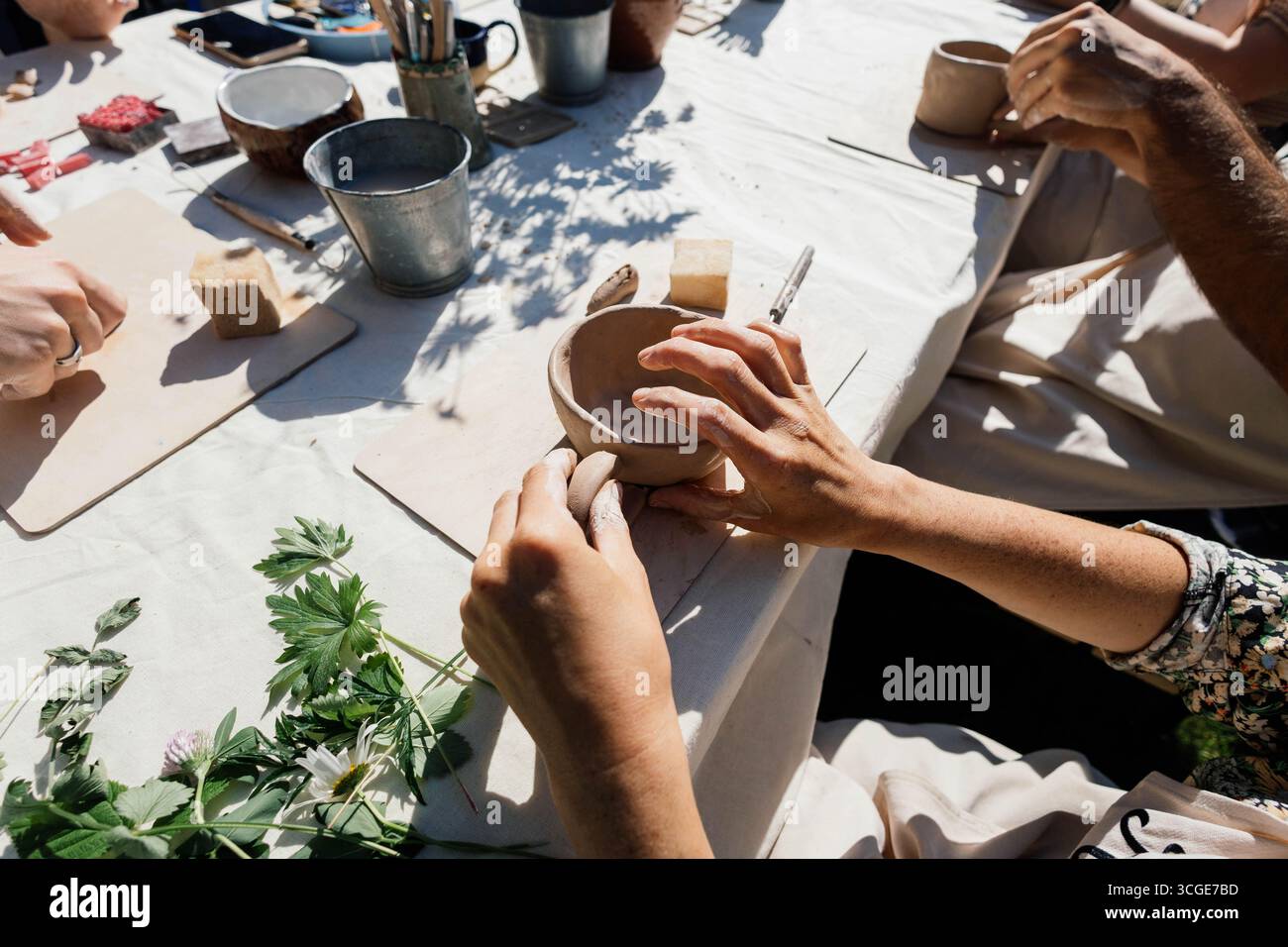 Les mains façonnent soigneusement l'argile en petits bols dans un atelier de fabrication de poterie tenu à l'extérieur. Les participants sont concentrés et apprécient le processus créatif sur Banque D'Images