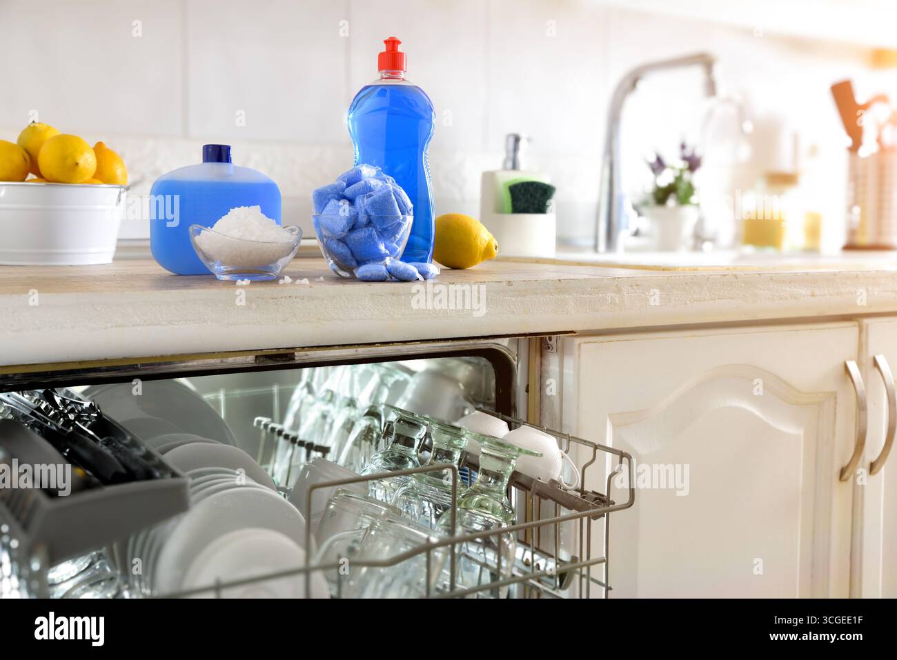 Détail d'un lave-vaisselle intégré dans une armoire de cuisine avec un plan de travail plein de produits pour le lavage et l'entretien du lave-vaisselle automatique. Vue de face. Banque D'Images
