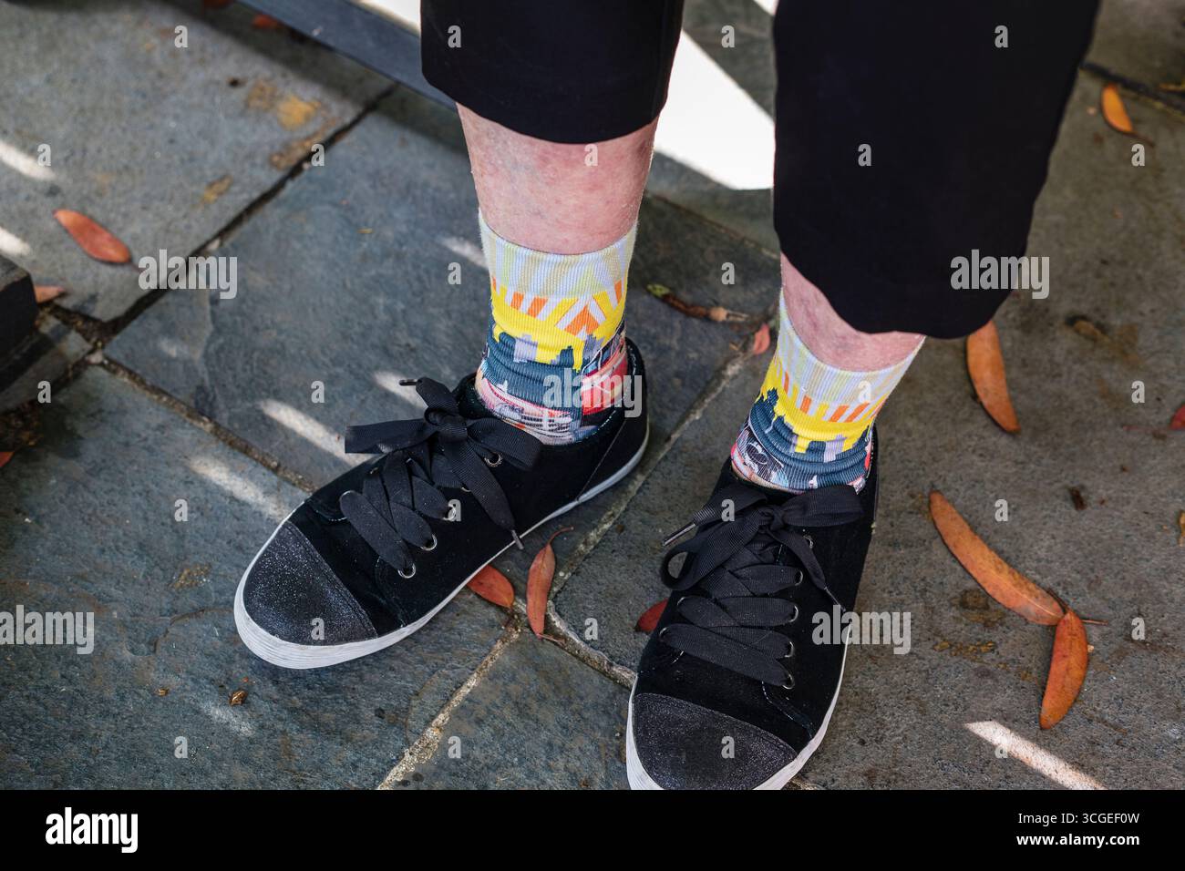Une femme âgée chevilles qui porte des baskets noires avec des chaussettes brillantes et funky et a une peau pauvre Banque D'Images